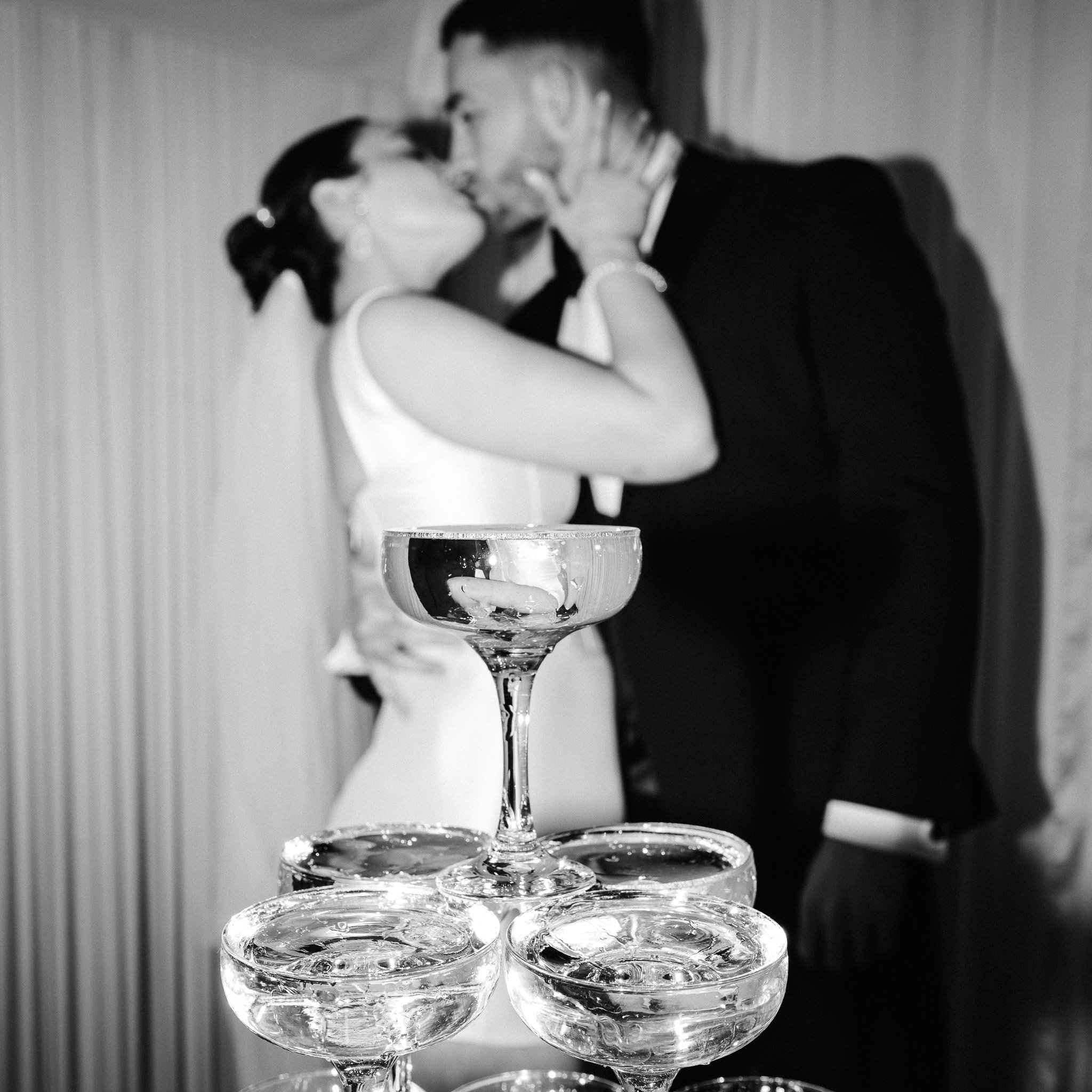 Hertfordshire Wedding Photographer - Shrigley Photography & Films - SHRIGLEY Bride & Groom kissing blurred out behind a champagne tower - Hertfordshire Wedding Photographer & Videographer - Shrigley Photography