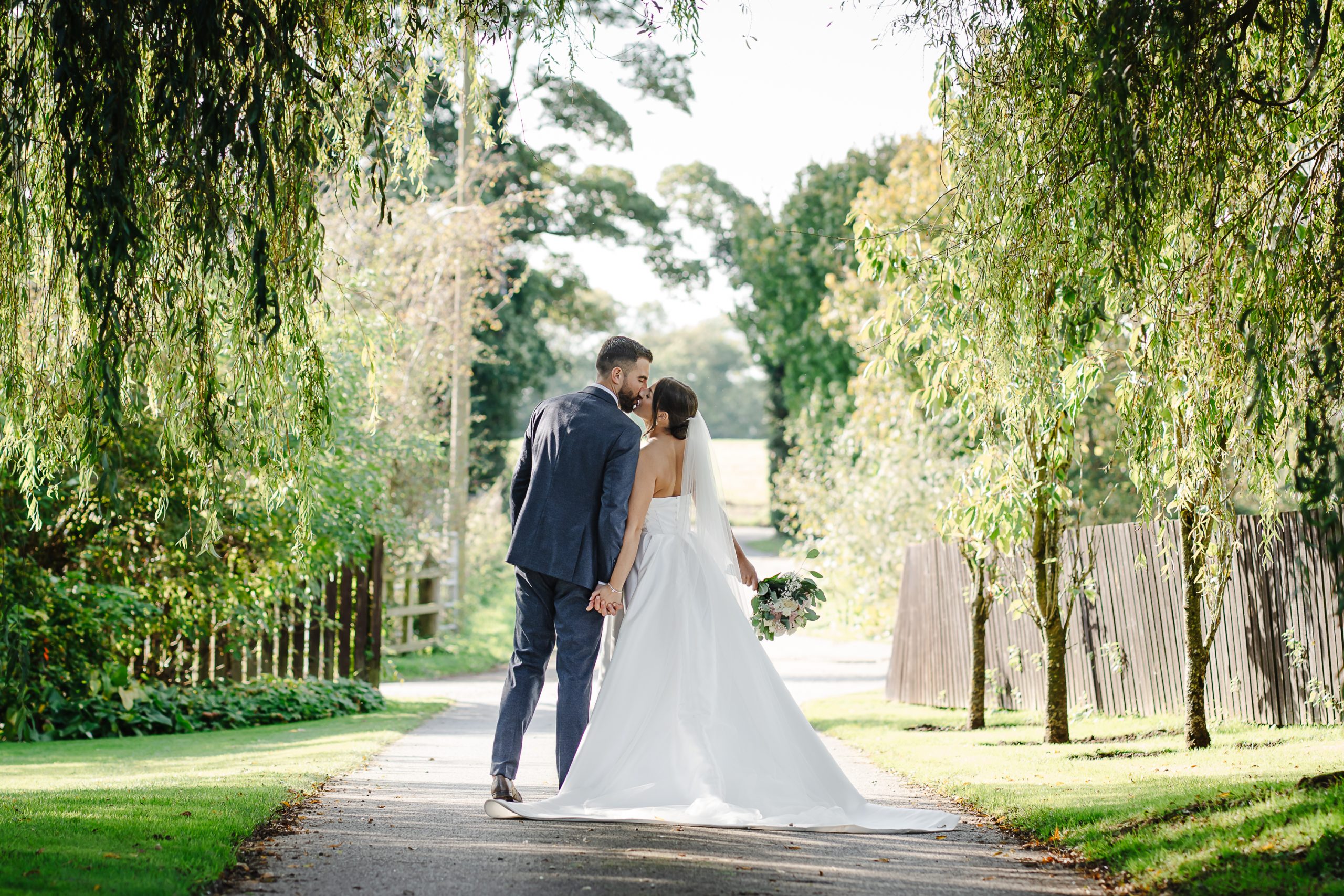 Editorial Wedding Photographer Hertfordshire | Shrigley Photography & Films - SHRIGLEY Bride & Groom kissing on a path lined with trees and grass - Editorial Wedding Photographer Hertfordshire | Shrigley Photography & Films