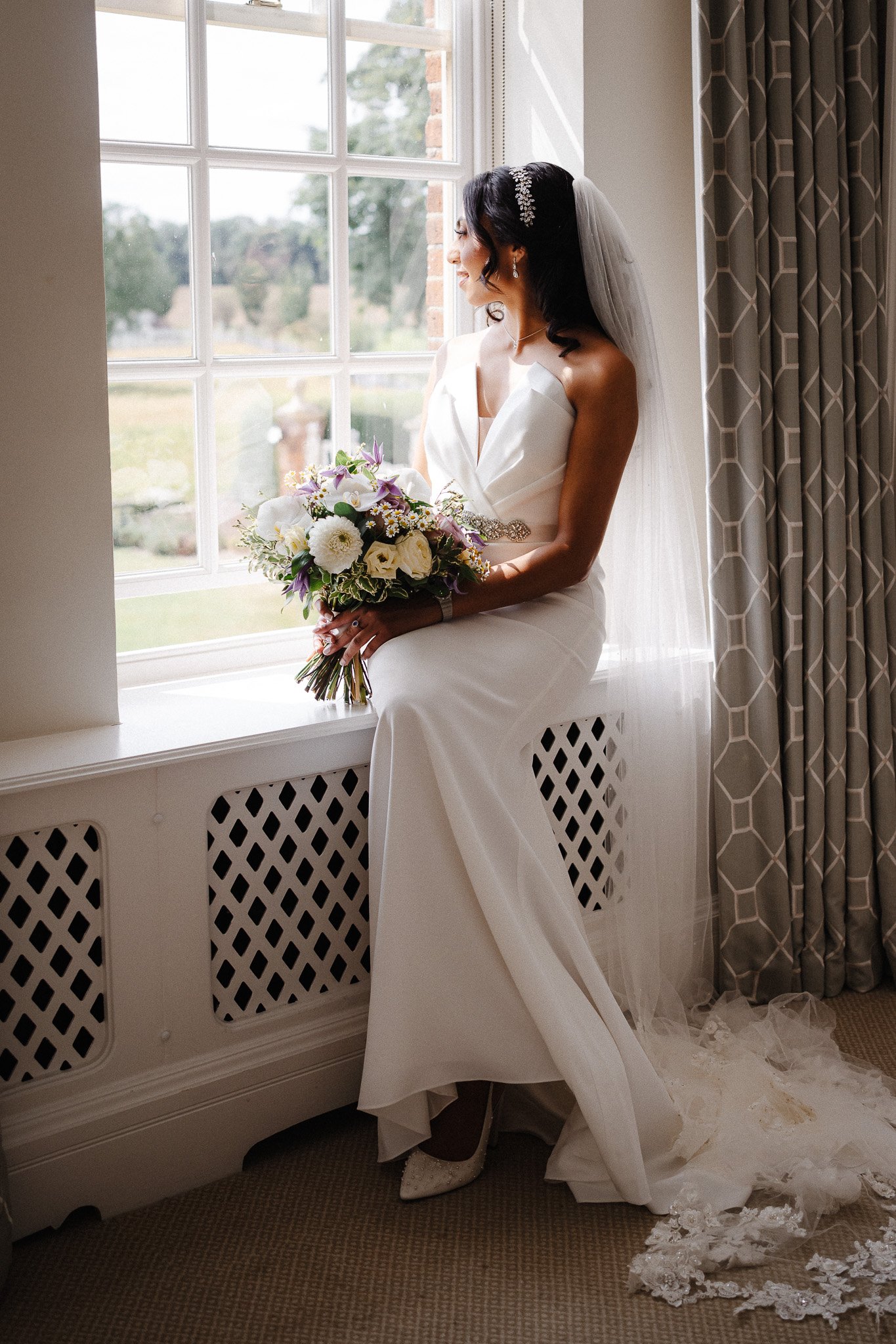 shrigley-photography-407470 - SHRIGLEY Bride sitting in a window in a cream dress looking outside holding her wedding bouquet of flowres - Hertfordshire Wedding Photographer & Videographer | Shrigley Photography & Film